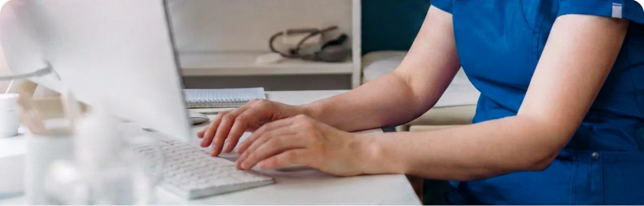 Healthcare professional in blue scrubs using a laptop to support virtual nursing workflows and hospital care coordination.