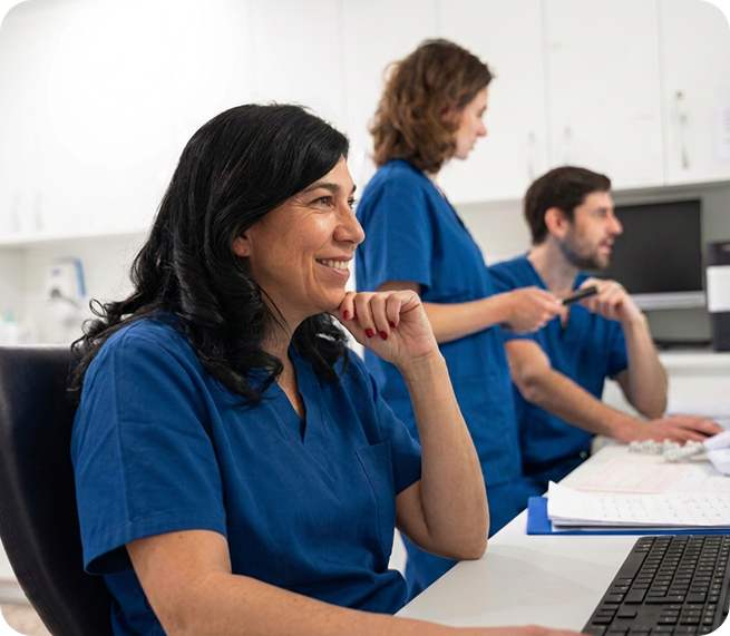 VirtuAlly healthcare professionals in blue scrubs collaborating at clinical workstations to support virtual nursing and hospital patient care.